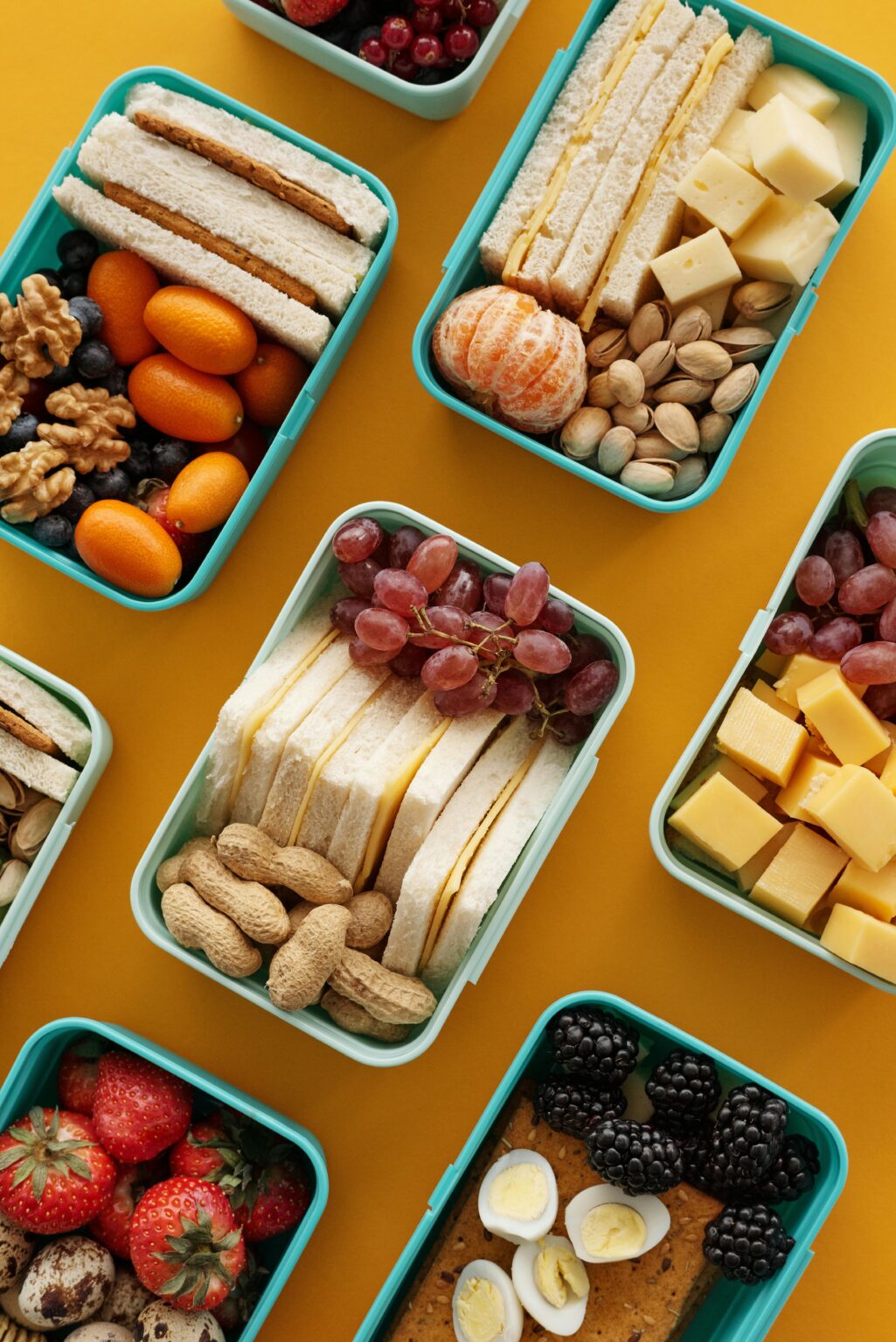 Top view of vibrant lunch boxes filled with assorted snacks on yellow background.