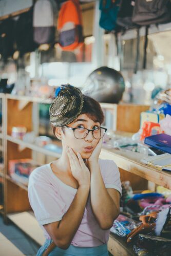 Playful portrait of a woman in a vintage shop wearing a unique hat and eyeglasses. Clothing persona- "Body Shape + Weight + Height"