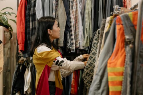 A young woman browsing clothes in a vintage store with colorful outfits...Clothing persona- "Body Shape + Weight + Height"